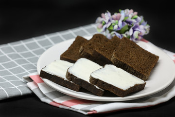 Brown bread with processed cheese on a plate and towels isolated on black background.