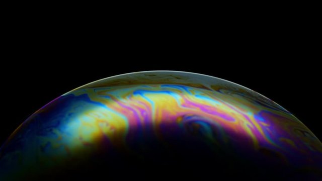 Multicolored rainbow iris of soap bubble. Fantastic colorful planet on black background. Abstract multi-colored surface overflows with abstract patterns