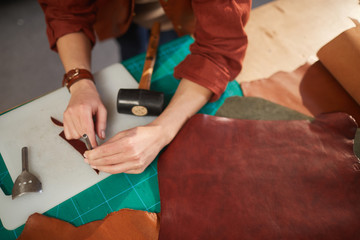 Horizontal from above shot of unrecognizable female artisan using leater punching tool on small detail