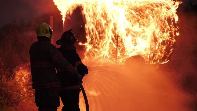 Rear view of Asian fireman wear fire protection suit. Firefighter spray water fighting at Fire station at night. Training fire drill Concept.