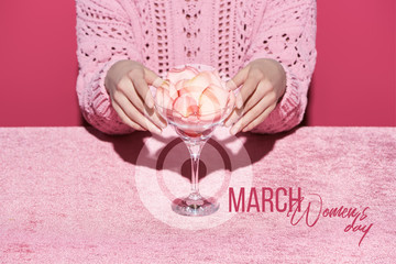 cropped view of woman with petals in glass on velour cloth isolated on pink, 8 march illustration