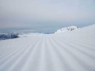 Snow velvet close up on ski slope on the background of snowy mountain peaks. Prepared ski and...