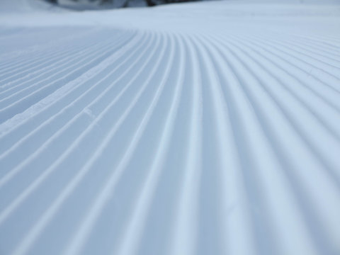 Snow velvet close up on ski slope. Prepared ski and snowboard track with trace of snow groomer on snow.