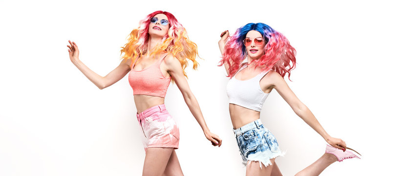 Two Young Woman with stylish pink blue hair, in fashion shorts jump dance. Beautiful fashionable cheerful swag cool girl in summer outfit. Friends with fashion dyed hairstyle jumping on white