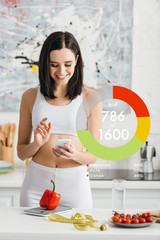 Smiling sportswoman using smartphone near measuring tape, vegetables and scales on kitchen table,...