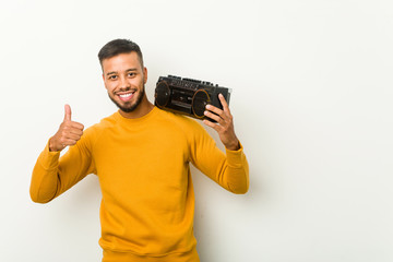 Young south-asian man holding a guetto blaster smiling and raising thumb up