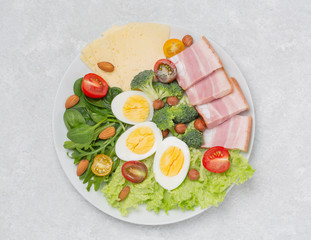 Plate with keto diet food. Keto breakfast: eggs, cheese, brisket, lettuce, broccoli, spinach, arugula, almonds, hazelnuts, blueberries and tomatoes.