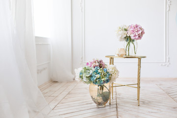 Tender simple  interior in light colors with tule, bouquets of artificial hydrangea and elegant  mirror table on light parquet floor