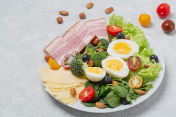Plate with keto diet food. Keto breakfast: eggs, cheese, brisket, lettuce, broccoli, spinach, arugula, almonds, hazelnuts, blueberries and tomatoes.