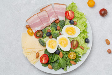 Plate with keto diet food. Keto breakfast: eggs, cheese, brisket, lettuce, broccoli, spinach, arugula, almonds, hazelnuts, blueberries and tomatoes.