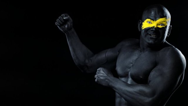 Man pick on copy space. Bodybuilder athlete with yellow face art and black body paint. Colorful portrait of the guy with bodyart.