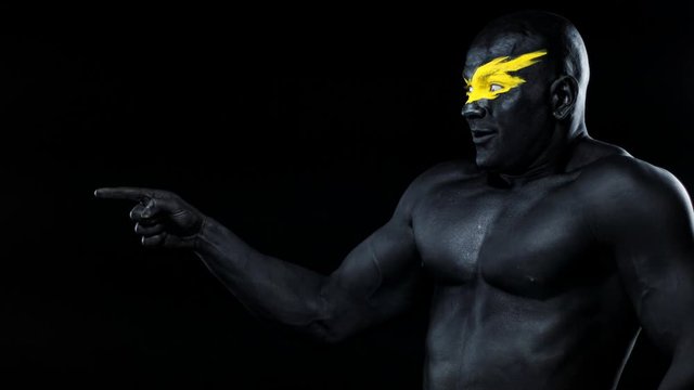 Man pick on copy space. Bodybuilder athlete with yellow face art and black body paint. Colorful portrait of the guy with bodyart.