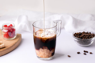 cold black coffee in a cup on a white background in which cream is poured