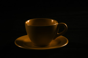 Yellow mug, cup silhouette on a black background. Low key photography close up