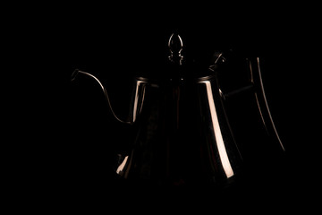 Silver teapot silhouette on a black background. Low key photography close up