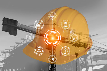 Double exposure engineering yellow hard safety hat and digital technology interfaces icon with construction cranes  background.