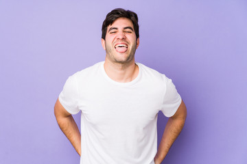 Young man isolated on purple background funny and friendly sticking out tongue.