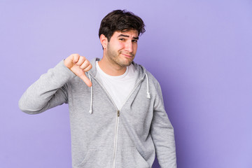 Young man isolated on purple background showing thumb down, disappointment concept.