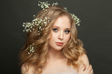 Perfect young woman with white flowers in blonde hair on dark background