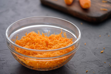 Juicy and fresh grated carrots on a wooden board on a dark background