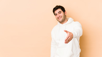Young man isolated on beige background stretching hand at camera in greeting gesture.