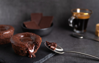 Warm chocolate lava cake on a black plate with a cup of coffee on a dark background