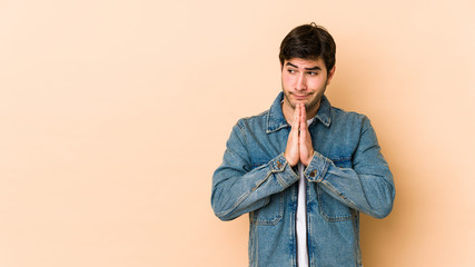 Young man isolated on beige background praying, showing devotion, religious person looking for...