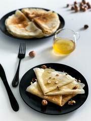 Crepes with honey and nuts, on a white plate, in black dishes. Homemade thin pancakes for breakfast or dessert.