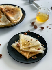 Crepes with honey and nuts, on a white plate, in black dishes. Homemade thin pancakes for breakfast or dessert.