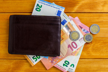 Various Euros banknotes, and coins on a wooden table, 5-10-20-50 EUR and a wallet.