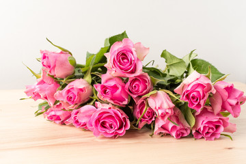 Side view of many small vivid pink rose flowers and green leaves on a raw wooden table, beautiful indoor floral background photographed with small focus