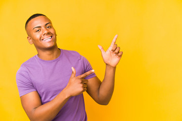 Young latin man isolated on yellow background pointing with forefingers to a copy space, expressing excitement and desire.