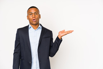 Young business latin man isolated on white background impressed holding copy space on palm.