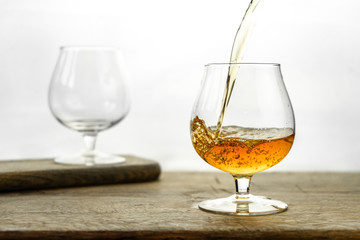 Cognac \ whiskey in cognac glass on wooden table, golden color spirits splashing on white background