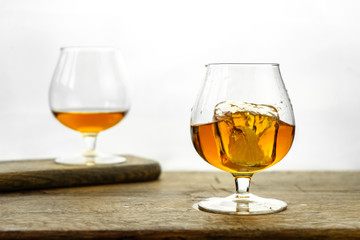 Cognac \ whiskey in cognac glass on wooden table, golden color spirits splashing on white background