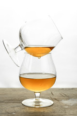 Cognac \ whiskey in cognac glass on wooden table, golden color spirits splashing on white background