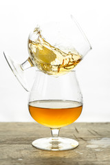 Cognac \ whiskey in cognac glass on wooden table, golden color spirits splashing on white background