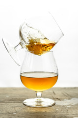 Cognac \ whiskey in cognac glass on wooden table, golden color spirits splashing on white background