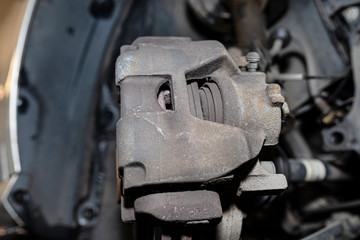 Front brake discs with brake caliper and brake pads in the car, on a car lift in a workshop.