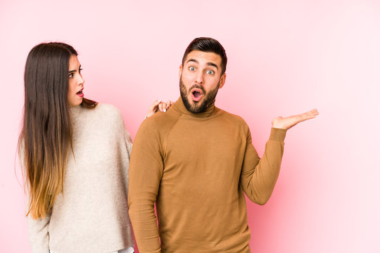 Young Caucasian Couple Isolated Impressed Holding Copy Space On Palm.