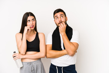 Young caucasian fitness couple isolated relaxed thinking about something looking at a copy space.