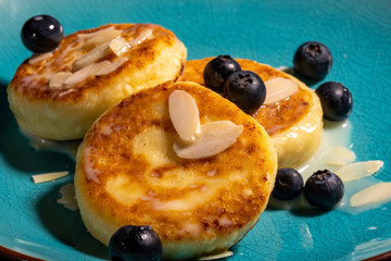 Cheese pancake with almonds and blueberries poured with condensed milk on a blue plate