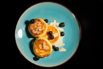 Cheese pancake with almonds and blueberries poured with condensed milk on a blue plate