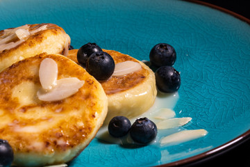 Cheese pancake with almonds and blueberries poured with condensed milk on a blue plate