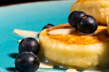 Cheese pancake with almonds and blueberries poured with condensed milk on a blue plate