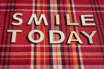 Smile today words written with wooden letters on red textile material with colored stripes, top view, flat lay