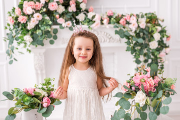 Beautiful little girl with a crown in a smart dress on a background of flowers