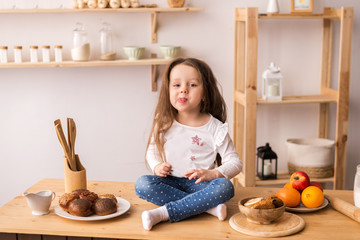 A smiling little girl sitting on the work surface of the kitchen waiting for breakfast. Cheerful and mischievous girl in the kitchen.