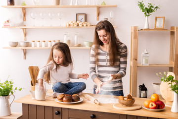 cheerful mother and daughter in the kitchen preparing Breakfast. Knead the dough from flour for pancakes, cookies and rolls. Flies flour and all laugh