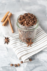 coffee beans in glass jar and cinnamon on light background